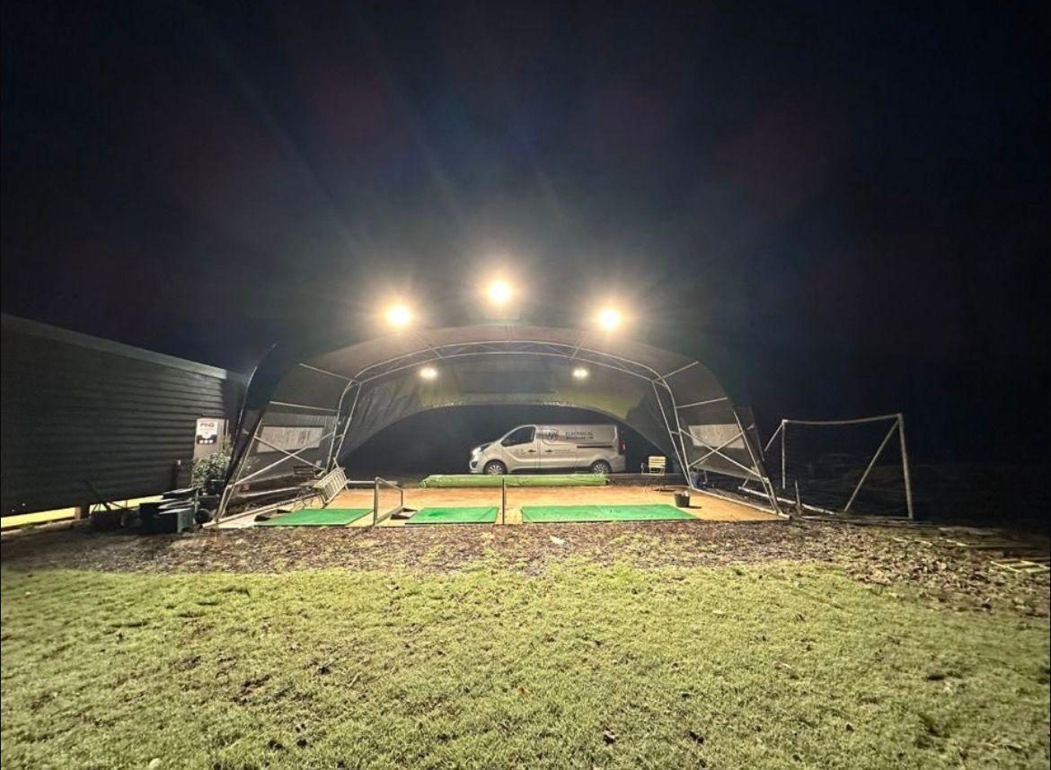 Wide shot of the covered driving range lit at night with the AW van inside